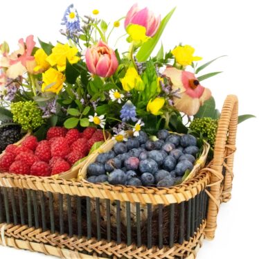 Detalle en ángulo de cesta de regalo con secciones de frambuesas y arándanos frescos y arreglo floral con tulipanes rosas.